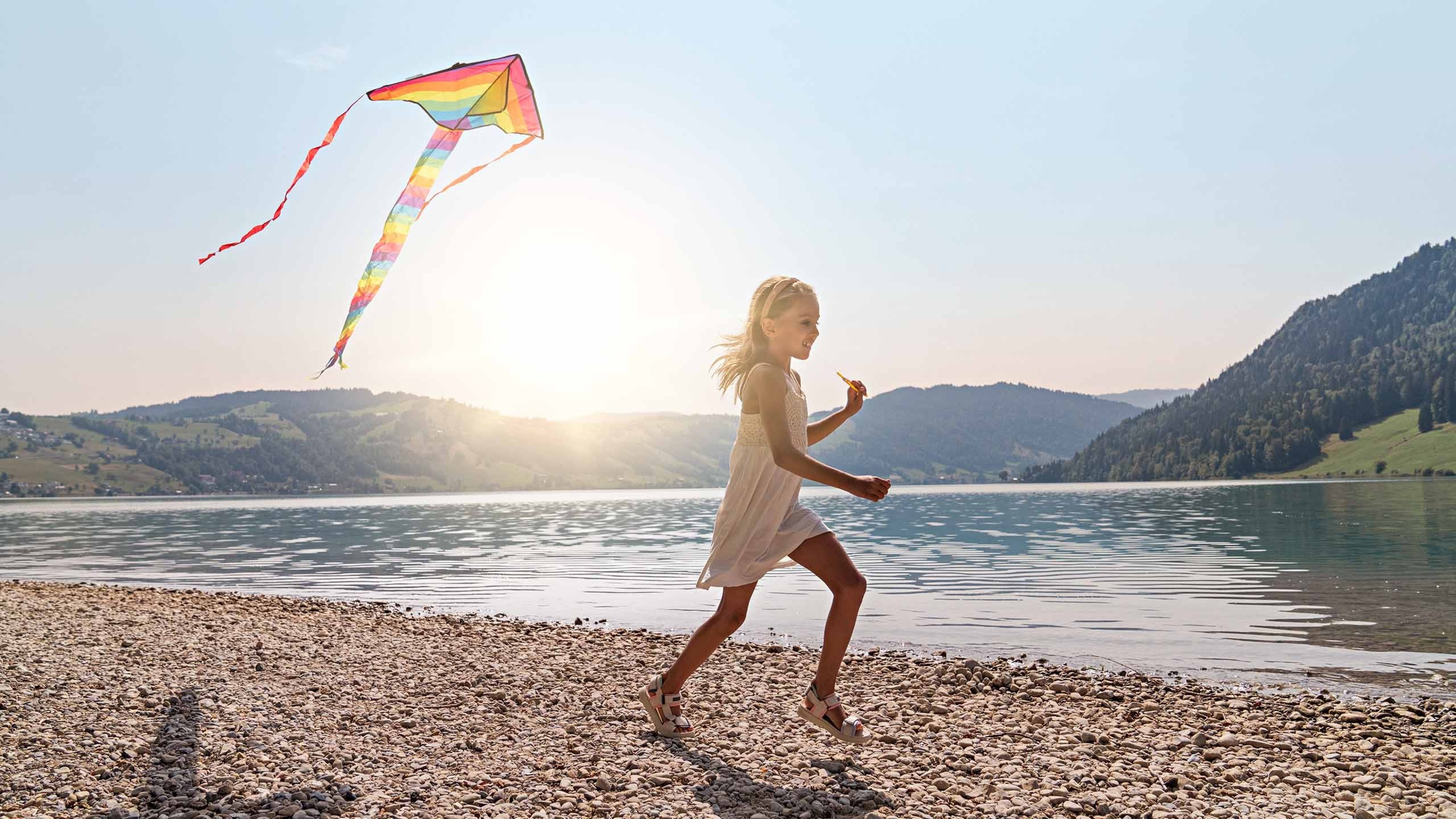 Une fille court le long des rives du lac et fait monter un cerf-volant.