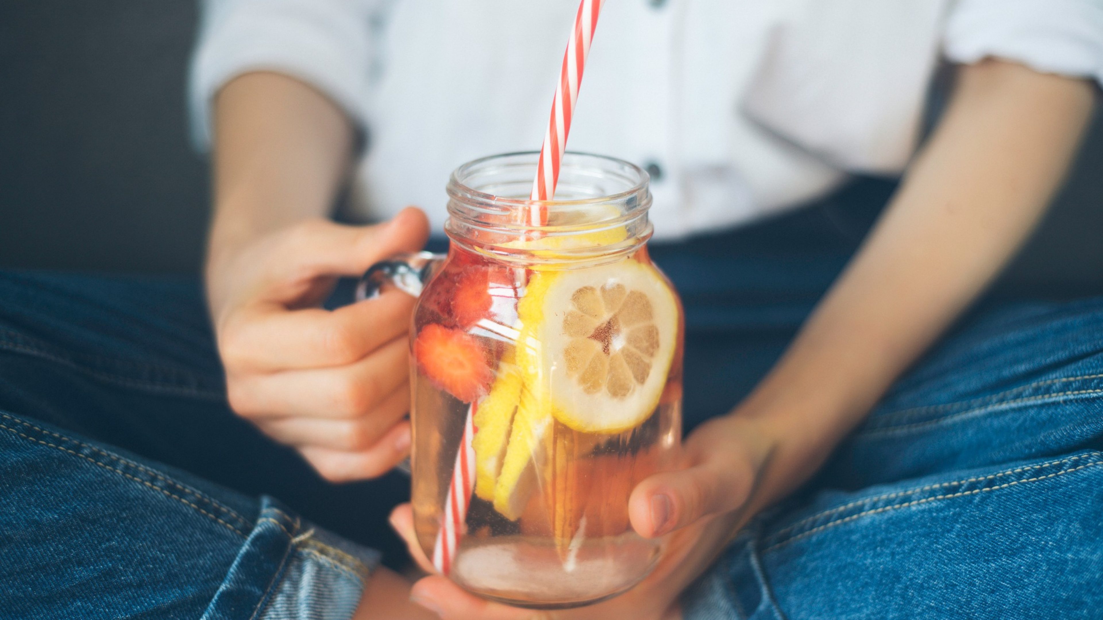 cropped shot of young woman drinking home made fresh summer drink from mason jar with straw