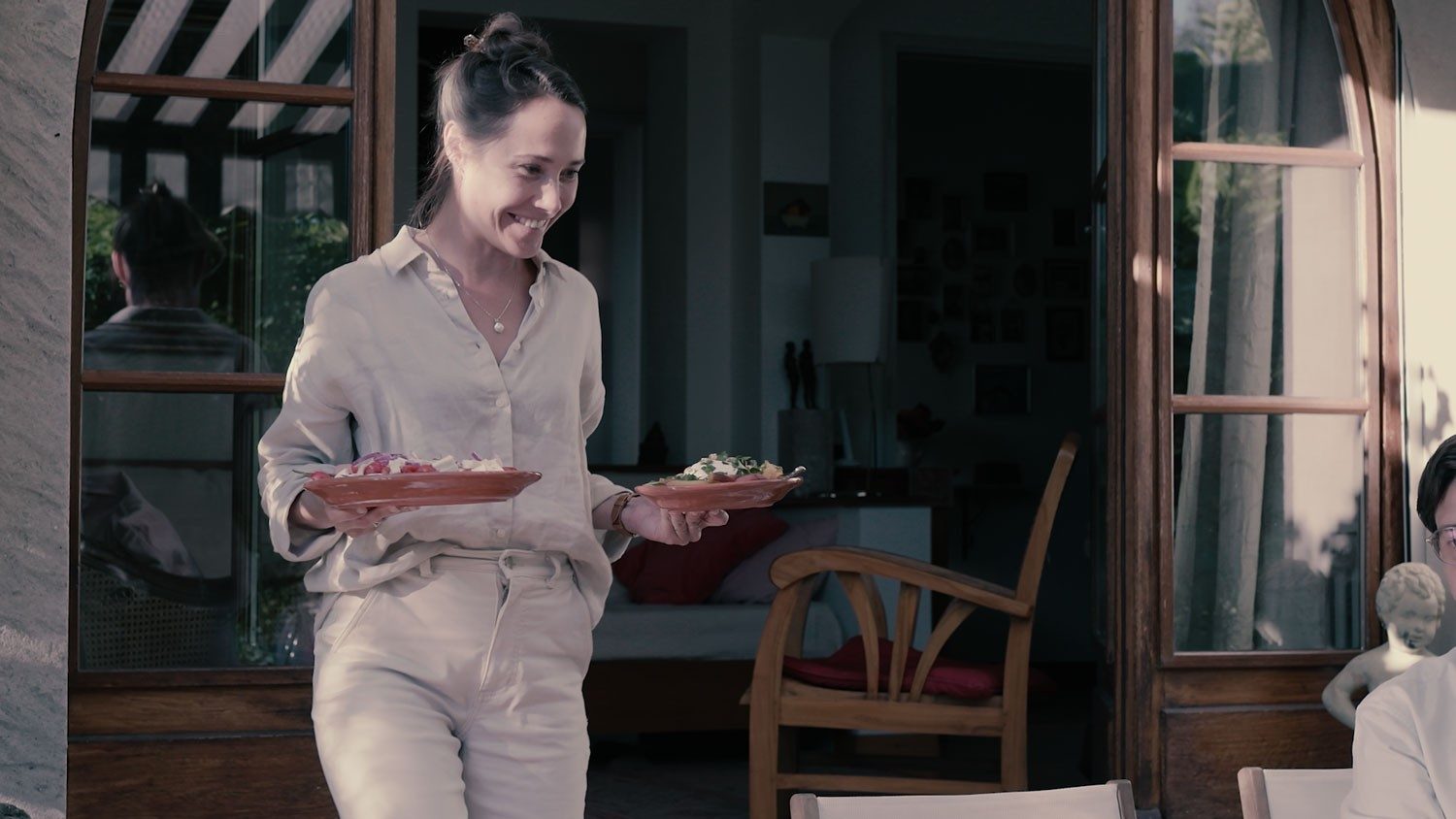 Una donna porta due piatti con del cibo in terrazza. 