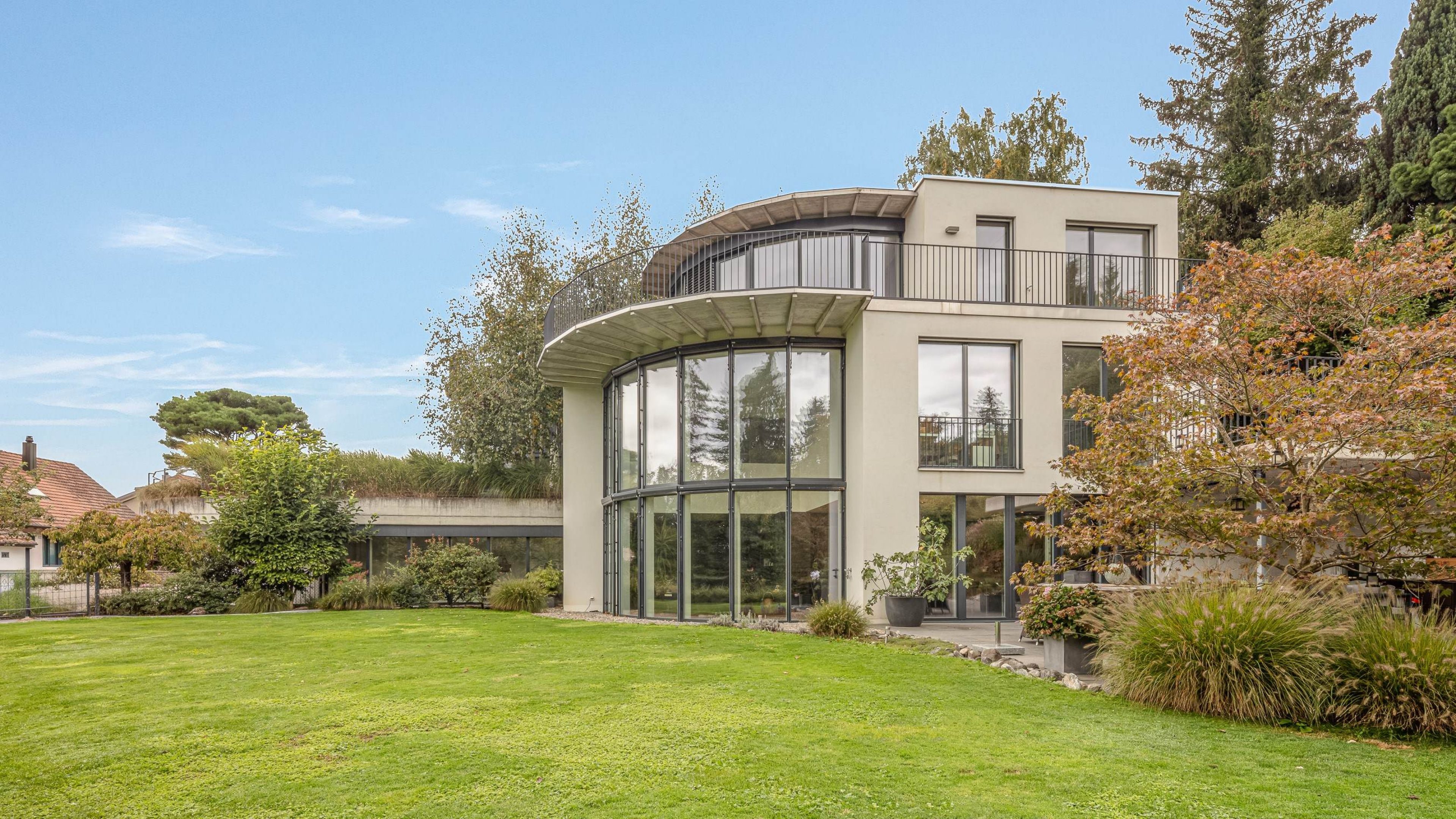 Moderna casa unifamiliare con grandi finestre in vetro, circondata da prato verde e alberi.
