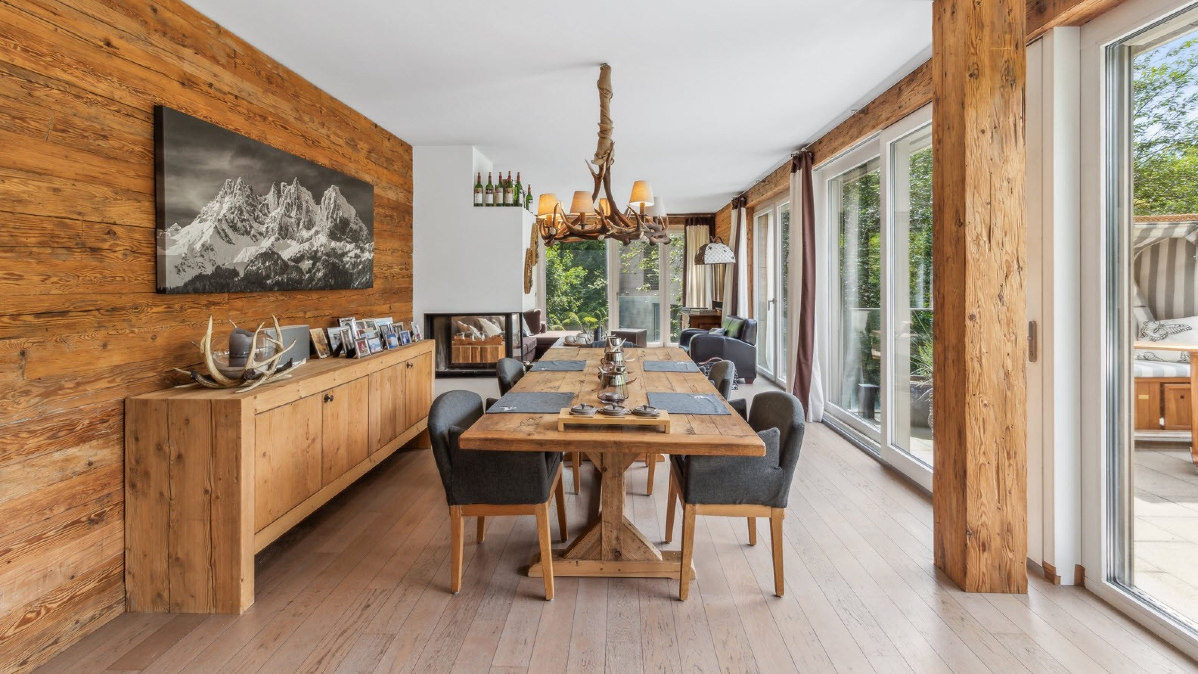 Grande sala da pranzo e soggiorno in stile rustico con tavolo apparecchiato in legno. Anche la parete sinistra e alcuni mobili sono in legno.