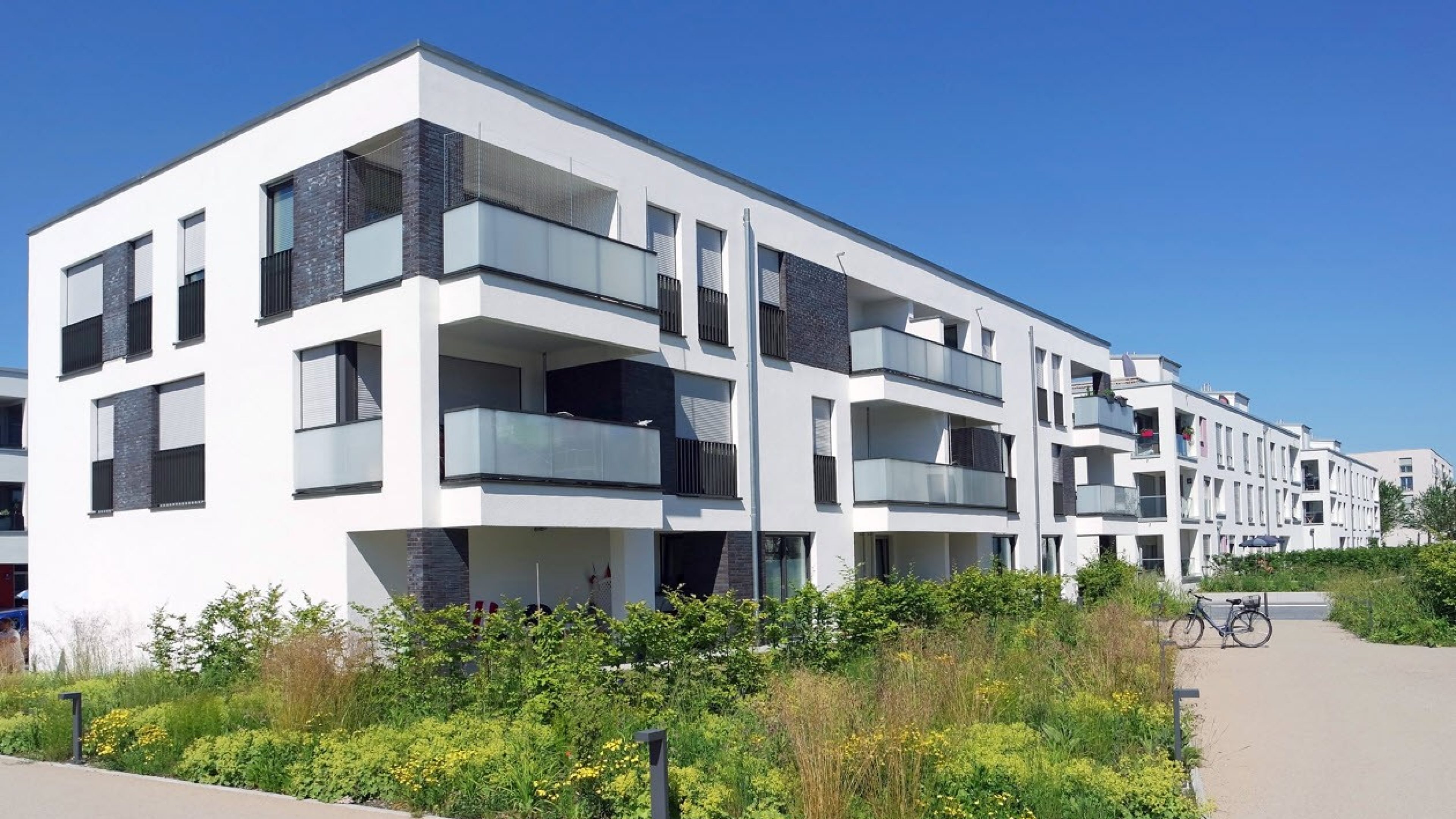 Moderne case plurifamiliari circondate da aree verdi e cielo azzurro. 
