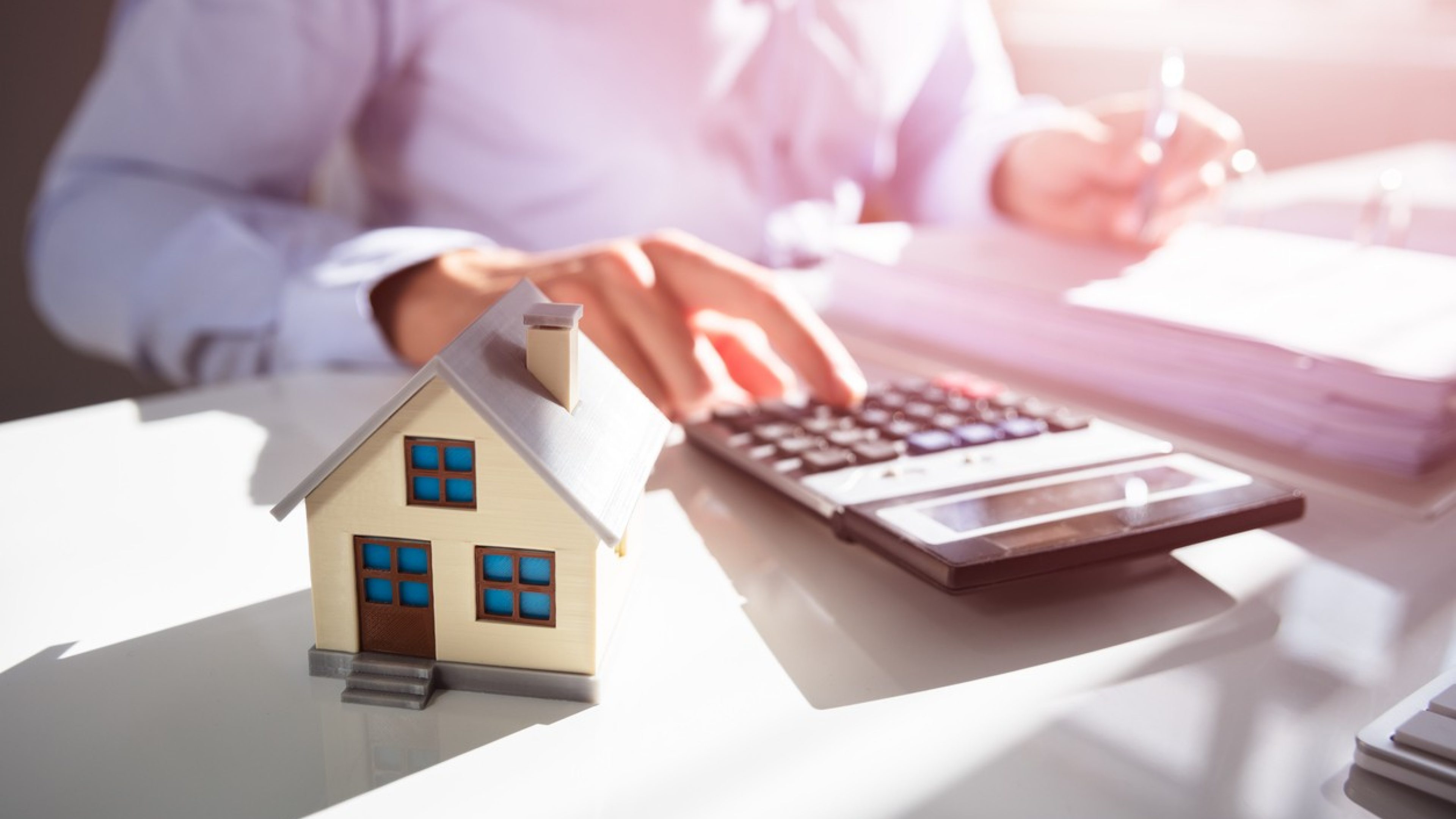 Close-up Of A Person Hand Doing Property Tax Calculation With House Model On The Table