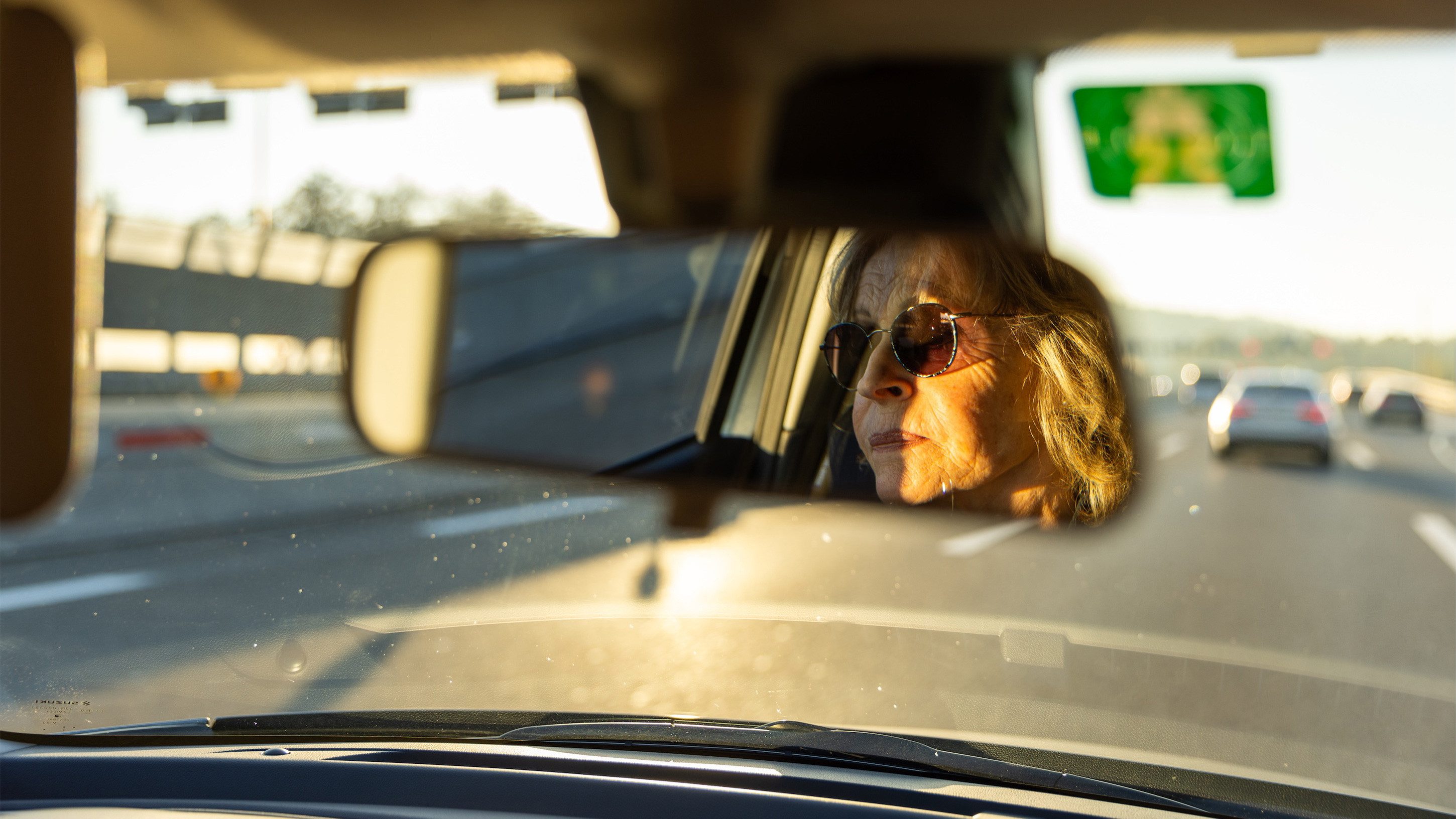 Fotografia Specchio retrovisore riflesso di una donna con occhiali da sole alla guida di un'automobile