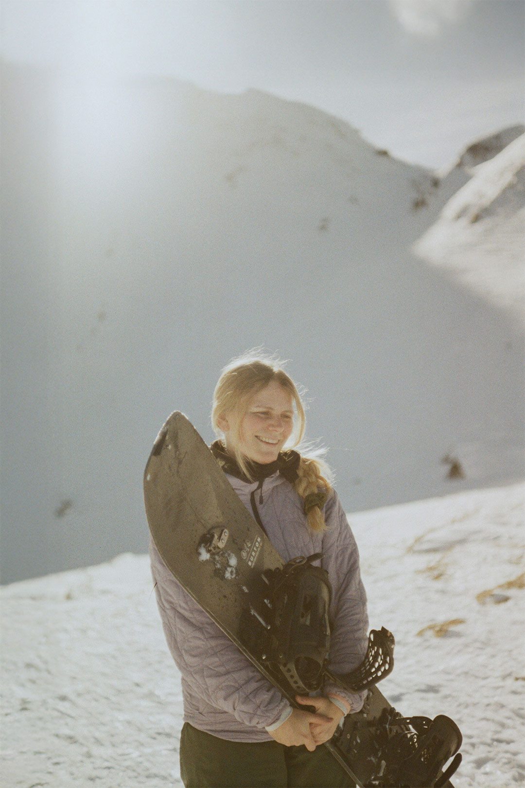 Persona con snowboard cammina su una cresta innevata in uno scenario alpino invernale.