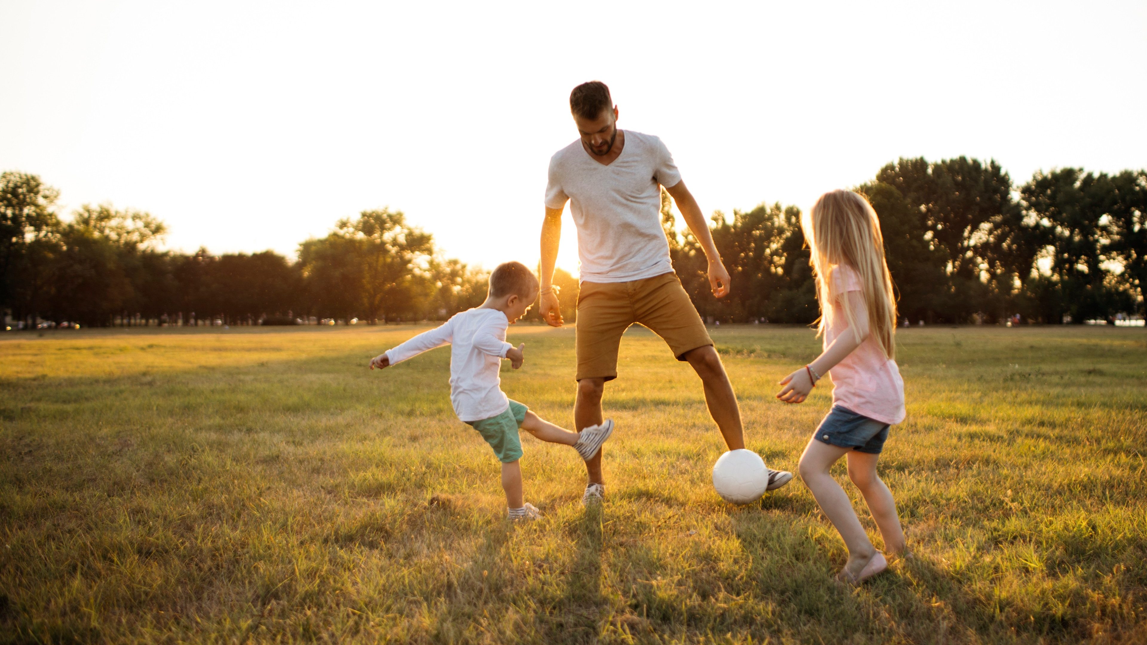 Kids and father playing soccer on a beautiful summer afternoon outdoors