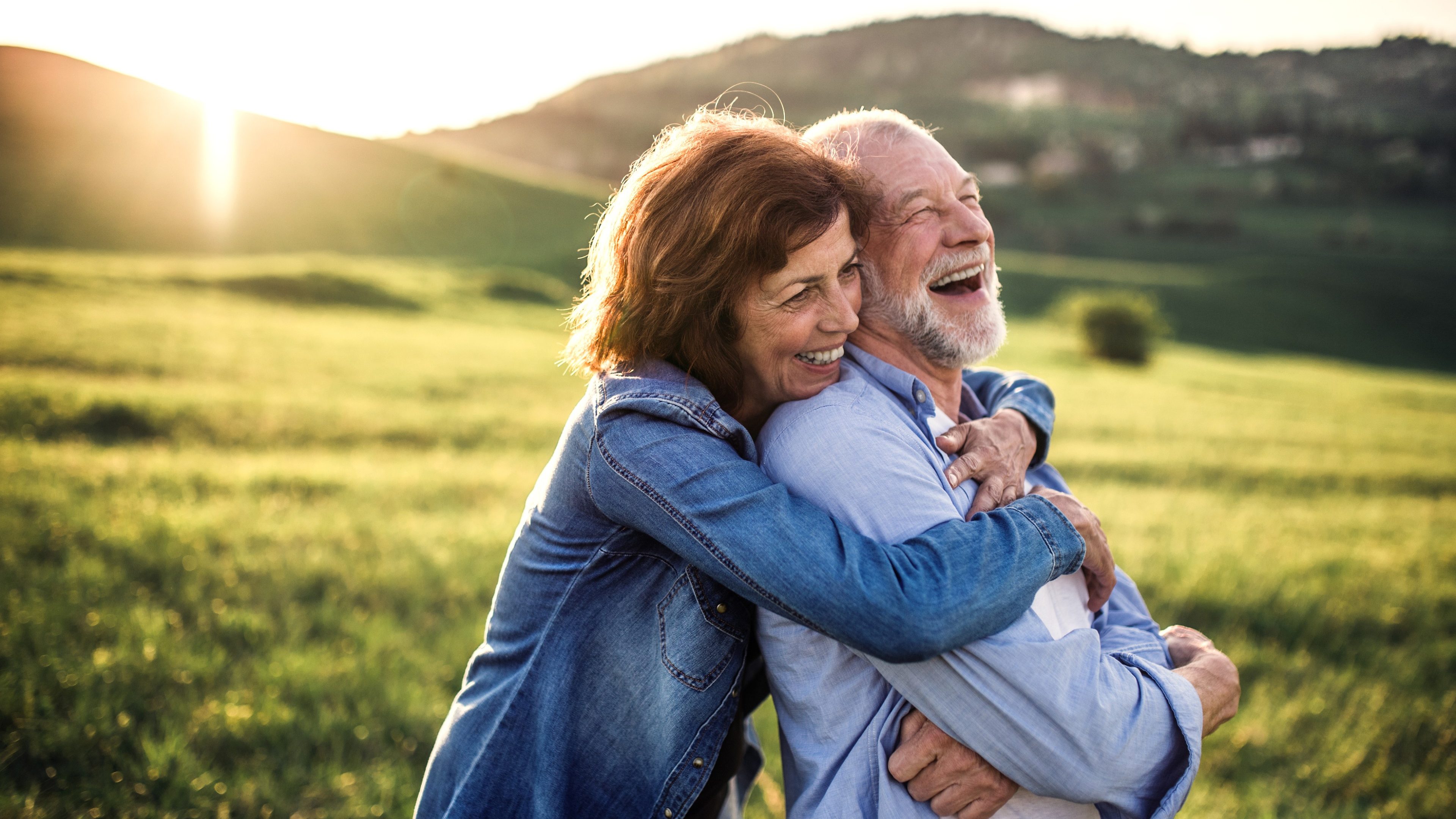 Happy senior couple outside in spring nature, hugging at sunset. Side view.