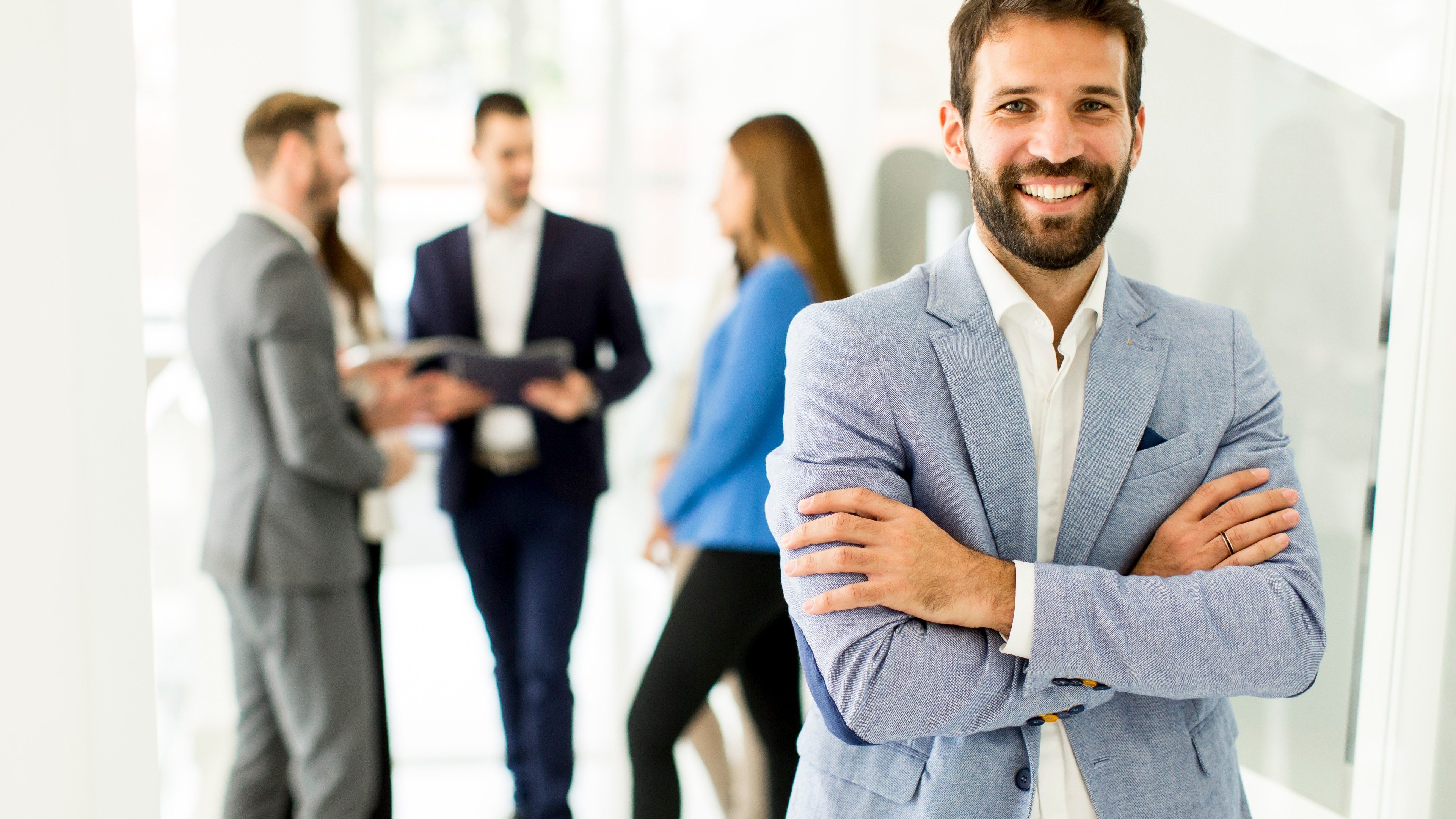 Young businessman standing in the office and other young business people talking in the background