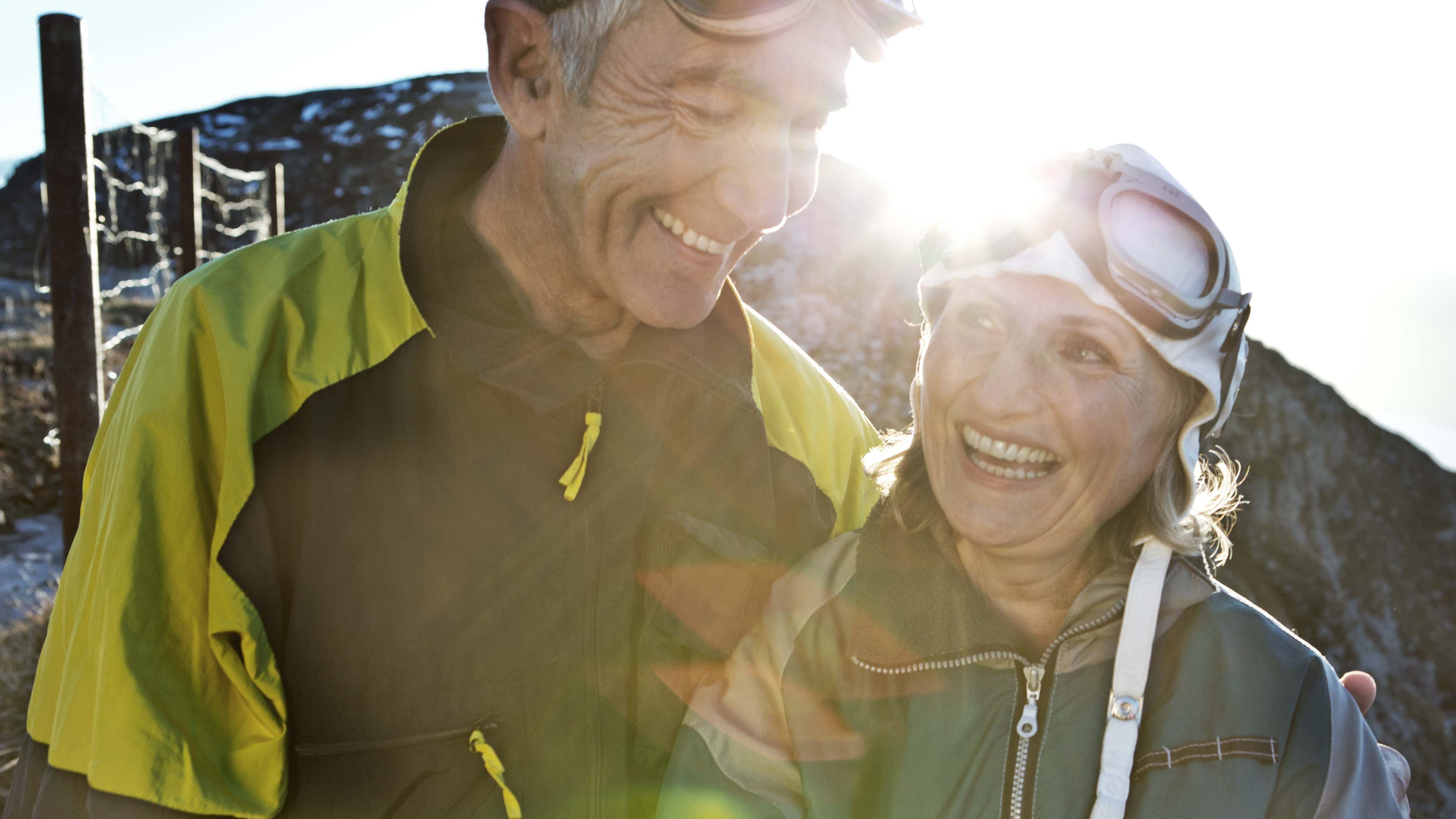 Due persone in abbigliamento outdoor davanti a una montagna, con la luce del sole dietro di loro