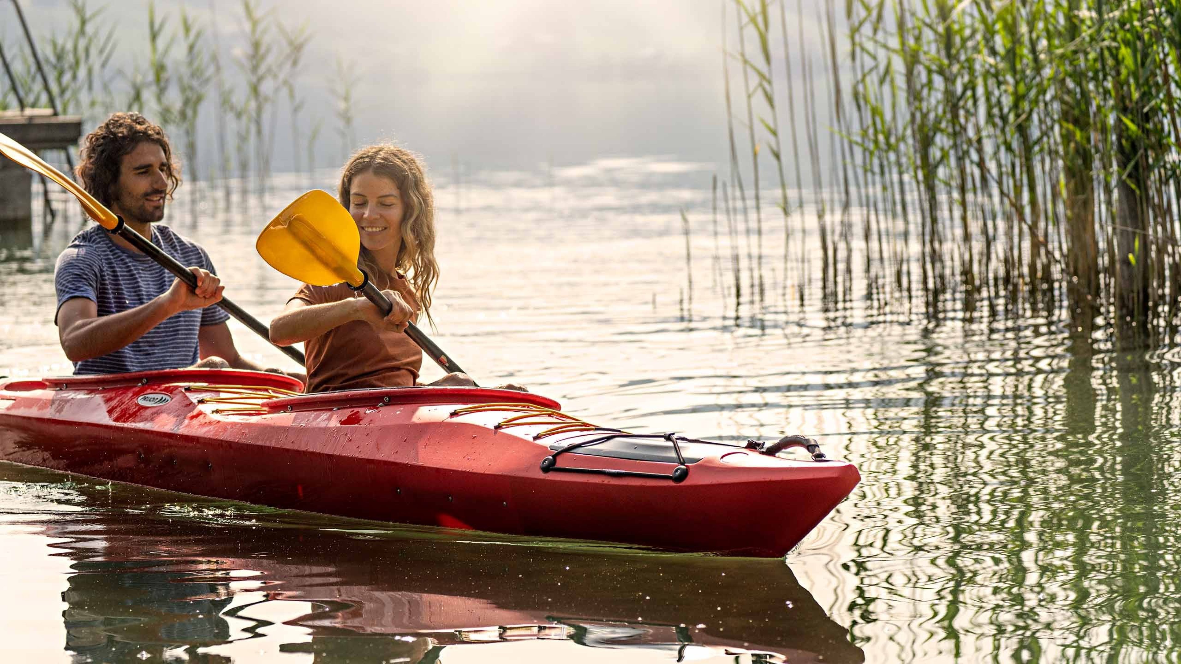 Una donna e un uomo stanno facendo canoa sul lago. Sullo sfondo si vedono delle canne.