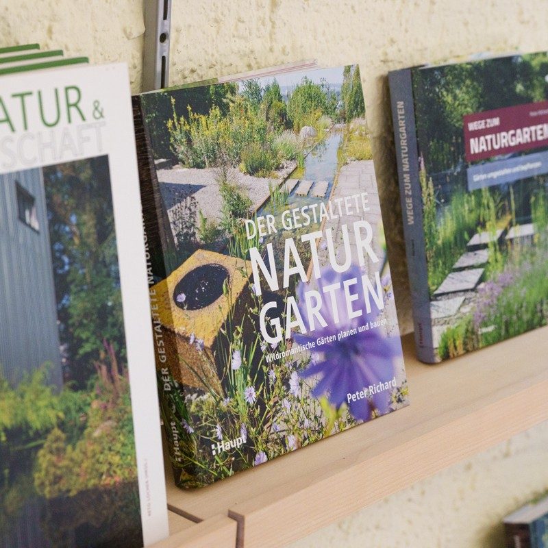 Due libri sui giardini naturali e un libro sulla natura e l’economia sono allineati su uno scaffale di legno.